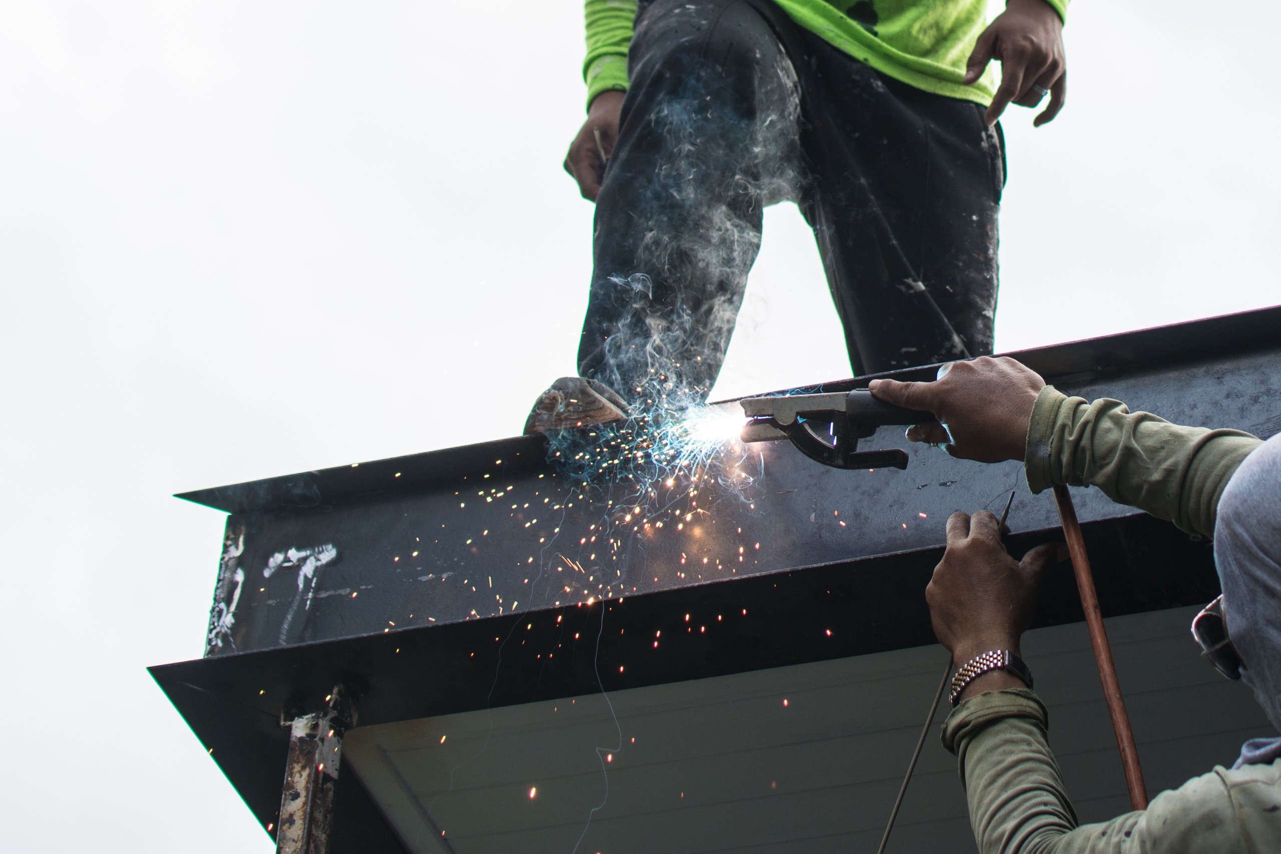 Worker welding steel structure of roof at construction site