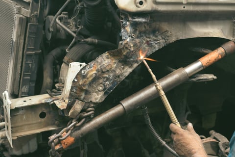 Mechanic welding a damaged car frame in an auto repair workshop