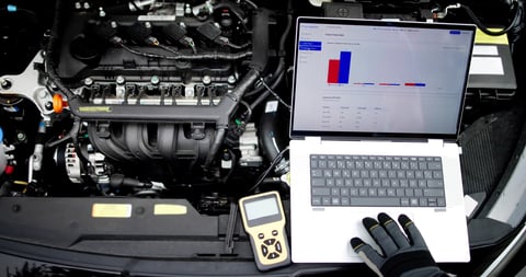 Senior mechanic analyzing engine issues with laptop in garage workshop