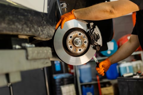 Mechanic hands with orange gloves installing car brake disc