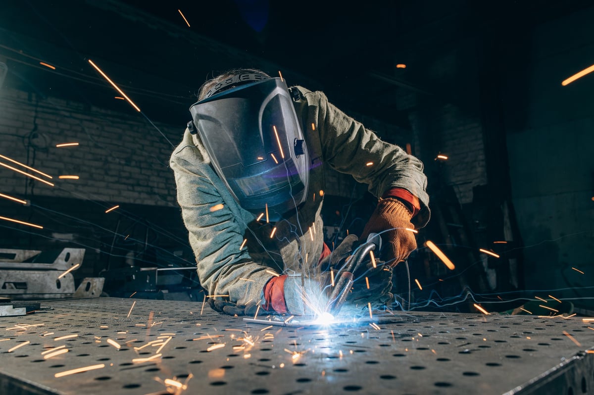 Professional metal worker welding steel in industrial workshop
