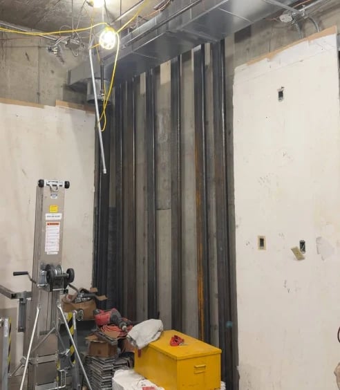 Construction site interior with exposed drywall, metal framing, work light, water heater, and yellow equipment storage box