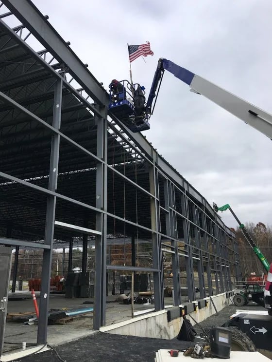 Workers on an elevated platform with American flag during construction of a large steel-frame building