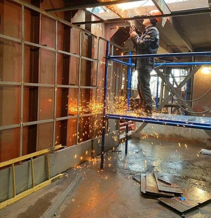 Worker welding metal on construction scaffolding with bright sparks and protective safety railings visible