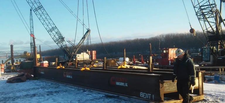 Large industrial barge with yellow cranes and equipment docked in frozen water, industrial facility in background